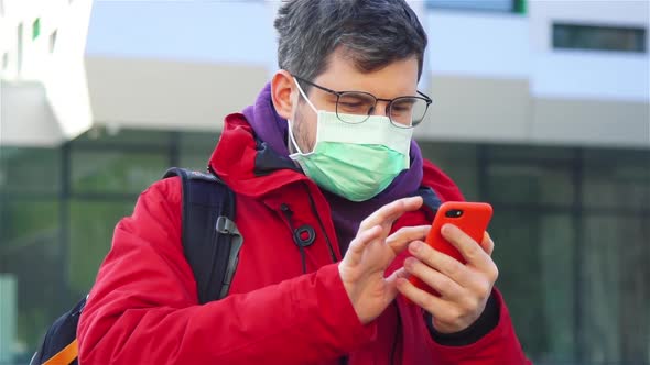 Man in Glasses Red Jacket and Respiratory Mask on the Street and Scrolling News