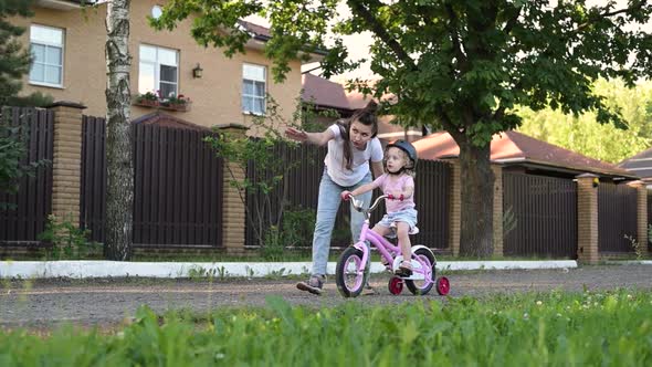 mother teaches her daughter to ride a bike. Little girl in helmet learns to ride