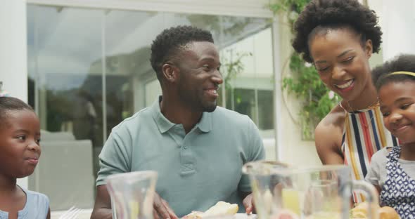 Happy african american family talking and having breakfast in garden