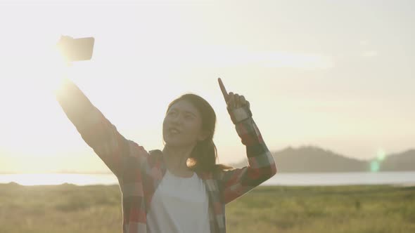 Attractive young Asian woman selfie video chat with her friends on the smartphone while sunset.