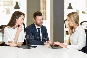  explaining with laptop computer to a smiling young couple.