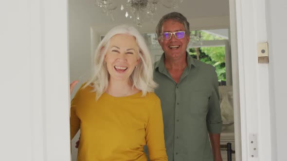 Animation of happy caucasian senior couple opening doors and welcoming friends