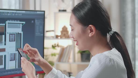 Close Up Of Asian Woman Engineer Using Smartphone While Designing House On A Desktop At Home