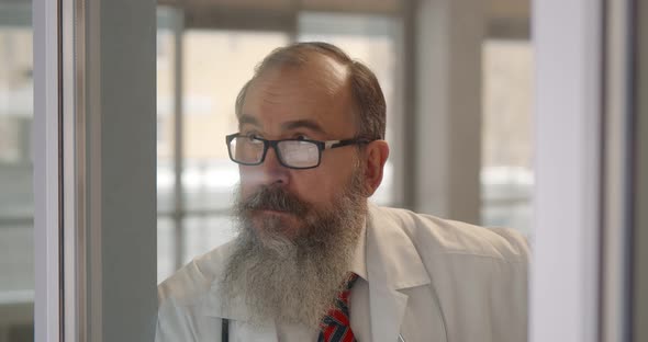 Tired Senior Man Doctor Standing Near Window in Clinic