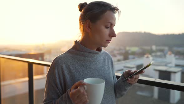 Woman Starts Her Day with a Cup of Tea or Coffee and Checking Emails in Her Smartphone on the