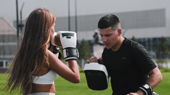 Young Woman with Long Hair Having a Boxing Training with Her Man Coach Punching in Mitts on His