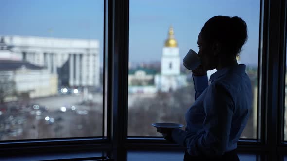 Woman Drinking Coffee Looking Out of Office Window