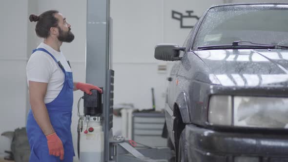 Adult Mechanic Lifts the Car Using Automatic Elevator. Worker Push the Button of Elevator To Lift