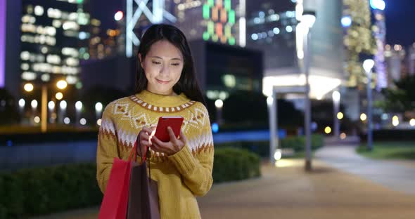 Woman use of mobile phone in city and hold with shopping bag at night