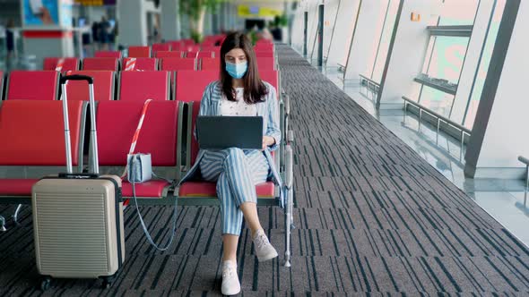 Woman in Protective Mask, with Luggage, Working on Laptop at Airport, While Waiting for Boarding