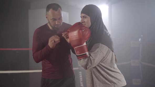 Positive Muslim Woman Standing in Boxing Stance As Caucasian Man Talking at the Background. Portrait