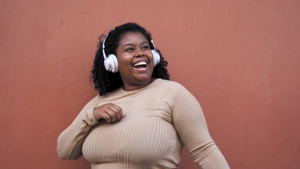 Happy Afro female having fun dancing and listening music with wireless headphones