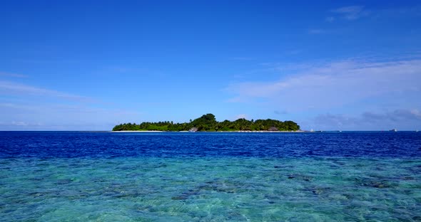 Wide angle fly over island view of a white sandy paradise beach and blue sea background in vibrant 4