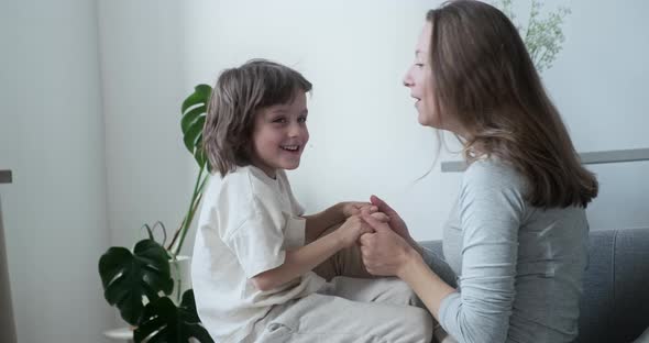 Blissful Joyous Happy Son Jumping Fun Playing and Embracing Young Mother Sitting on Couch