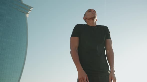 Pretty bald sportsman wearing black t-shirt does shoulders warm-up outdoors
