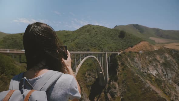 Back View Young Traveler Woman Hiking with Backpack Takes Smartphone Photos