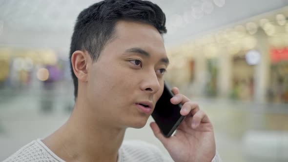 Close Up of Asian Male Talking on Phone on Shopping Center Background