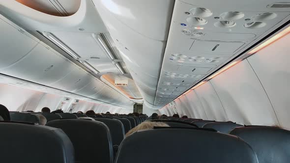 View of the Aircraft Cabin and the Back Side of the Seats with People Sitting in Them