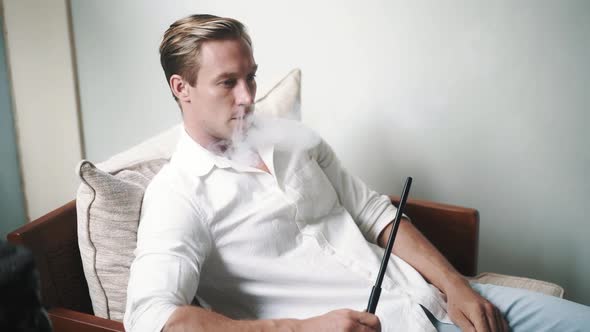 Slowmotion Video of Caucasian Young Man Smoking Hookah on Sofa