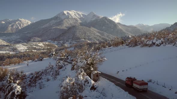 Aerial view of a car road surrounded by snow and pine trees in Greece.