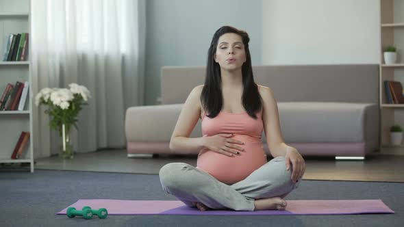 Pregnant Woman Sitting on Yoga Mat Doing Breathing Exercises and Massaging Belly