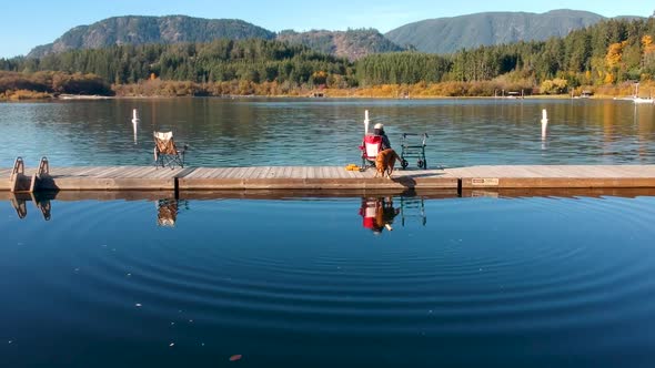 Dog jumping in lake while man fishing on dock in autumn