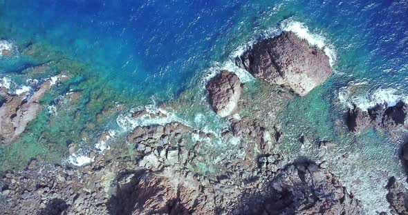 Aerial top view of waves break on rocks in a blue ocean. Sea waves on beautiful beach aerial view