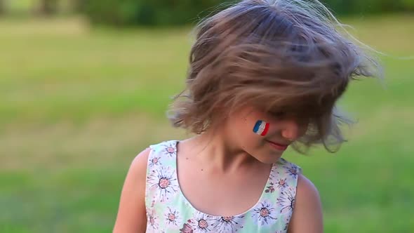 Child Cheerful Girl Happily Shakes Head with Her Cheeks Painted in the Flag of France Her Hair