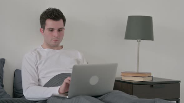 Man Celebrating Success on Laptop in Bed
