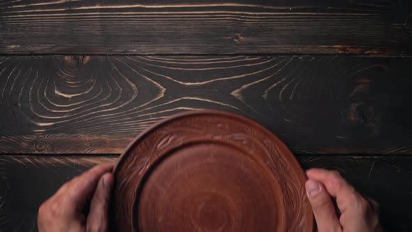 Male Hands Puts and Takes Away Empty Ukrainian Clay Plate From Wooden Table