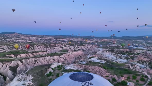 Hot air balloons fly over the mountainous landscape of Cappadocia, Turkey.