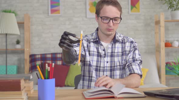 Young Man with a Bionic Prosthetic Hand Makes Notes in a Notebook