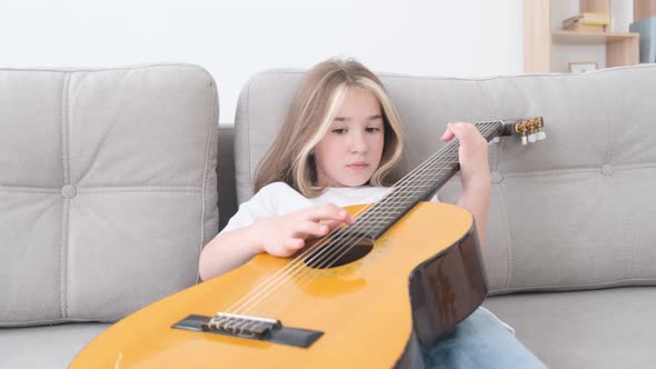 Sad Little Girl Playing Guitar She is Resting Sitting on the Couch at Home