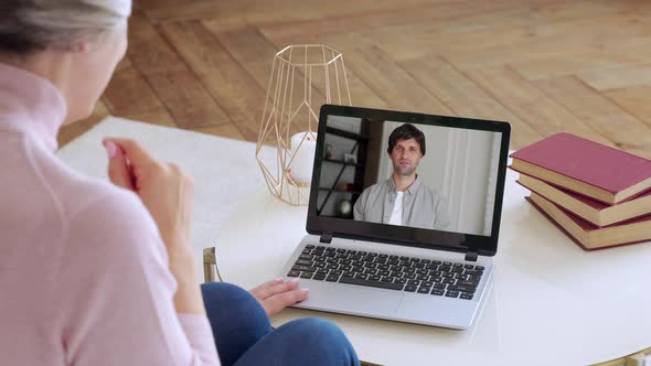 Over the Shoulder View of an Elderly Woman Video Call To a Young Son Using a Laptop. The Concept of