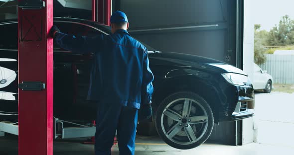 Car Service Worker Lifting Vehicle on Hoist Before Maintenance at Service Workshop