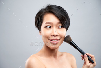 ng powder with make-up brush on her face isolated on grey background