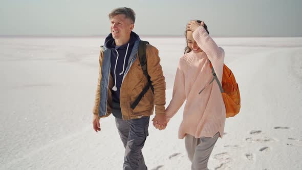 Happy Lovely Couple Travelers Walking Hand to Hand on Pink White Salty Coast