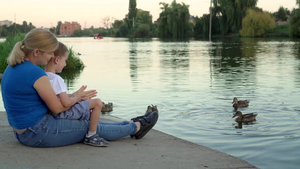 Mother and Child in Medical Masks Feed Ducks on the Lake