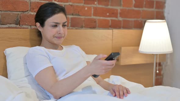Young Indian Woman Watching TV while Sitting in Bed