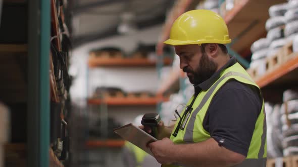 Caucasian male factory worker at a factory wearing a hard hat and high vis vest, checking stock