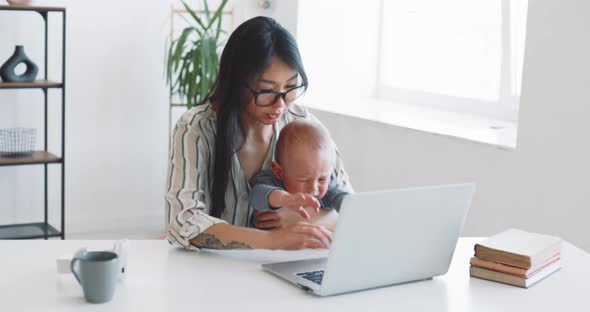 Young Mother Freelancer with Her Child Working at Home Office Using Laptop