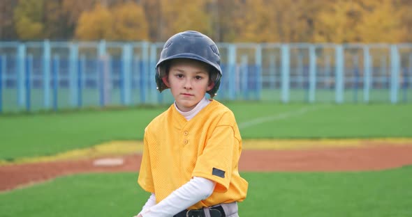 Portrait of a Boy Baseball Player on a Blurry Background, the Batter Holds a Baseball Bat in His