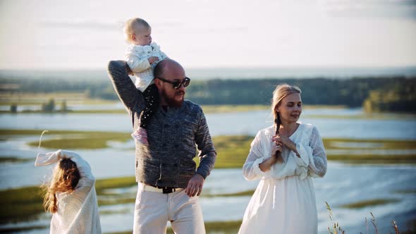 Young Family Standing on the Field Near the River - a Little Baby Sitting on Her Father's Shoulders