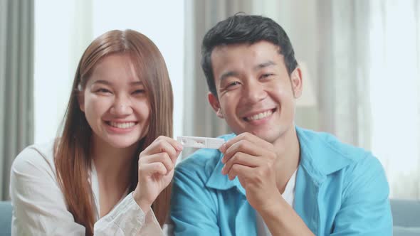 Close Up Happy Asian Couple Holding Positive Pregnancy Test And Smiling To Camera At Home