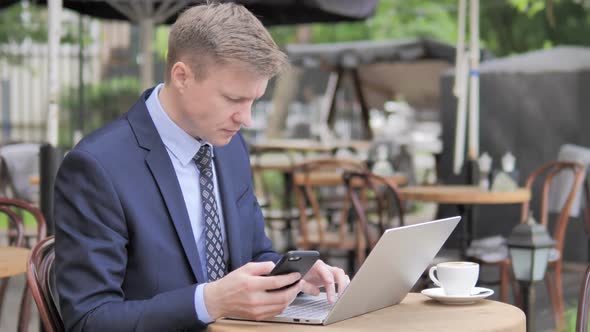 Businessman Using Smartphone and Laptop in Outdoor Cafe