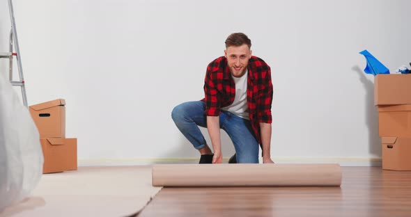 A Young Man Unfolds a Roll of Construction Cardboard to Protect the Floor From Painting