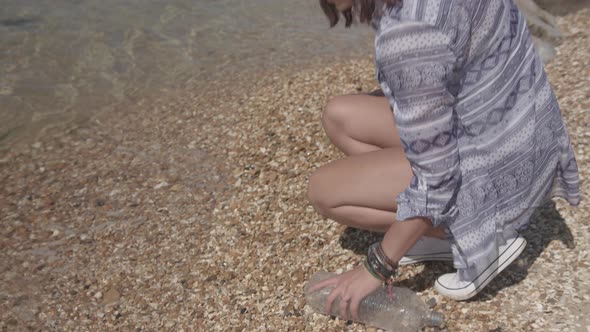 Close Up Shot Of Young Woman Reaching Down To Pick Up Plastic Bottle On Beach In Slowmotion - Ungrad