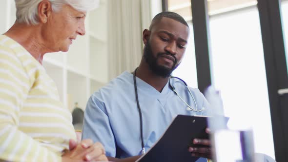 Video of african american male doctor using tablet giving medicines to caucasian senior woman