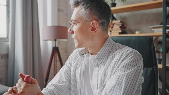 Close Up Portrait of Pensive Middle Aged Man in Eyeglasses Sitting at Wokplace and Rubbing Hands