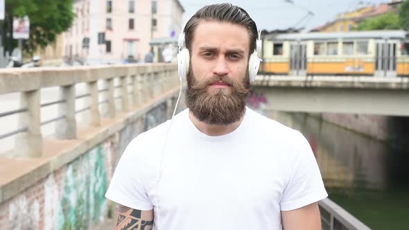 slow motion portrait young beautiful bearded man outdoor listening music looking camera